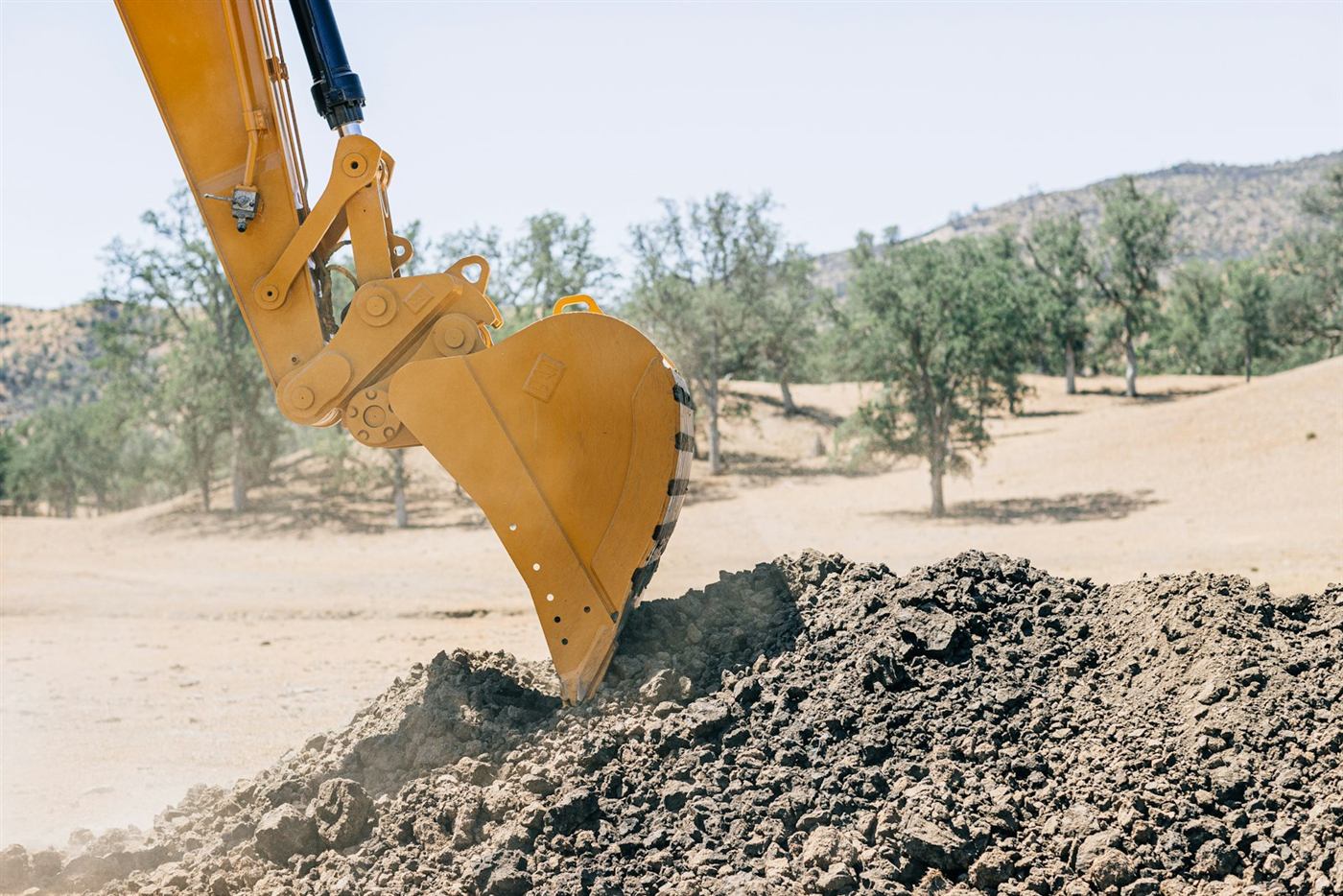 Excavator bucket moving soil on rural land during site work