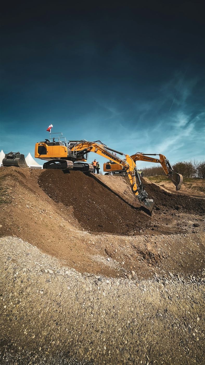 Two excavators positioned on a graded earth mound at a construction site