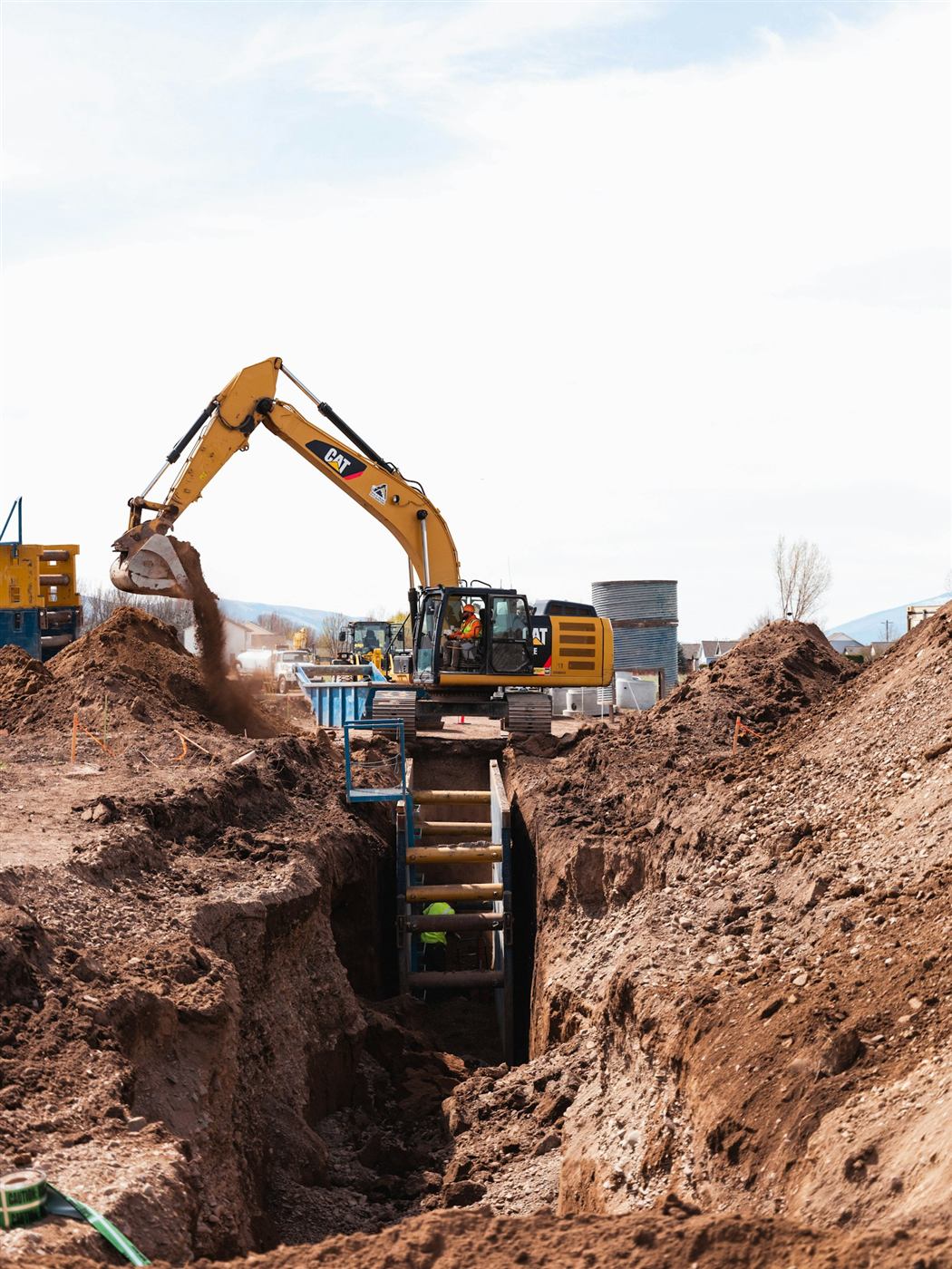 Yellow excavator working beside an open trench for utility line excavation